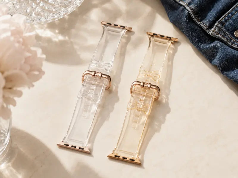 Clear and mildly yellowed transparent bow Apple Watch bands shown side by side near dark denim