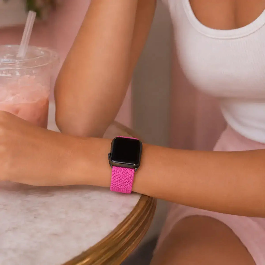 Close-up of a fuchsia braided Apple Watch band worn at a café table