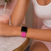 Close-up of a fuchsia braided Apple Watch band worn at a café table