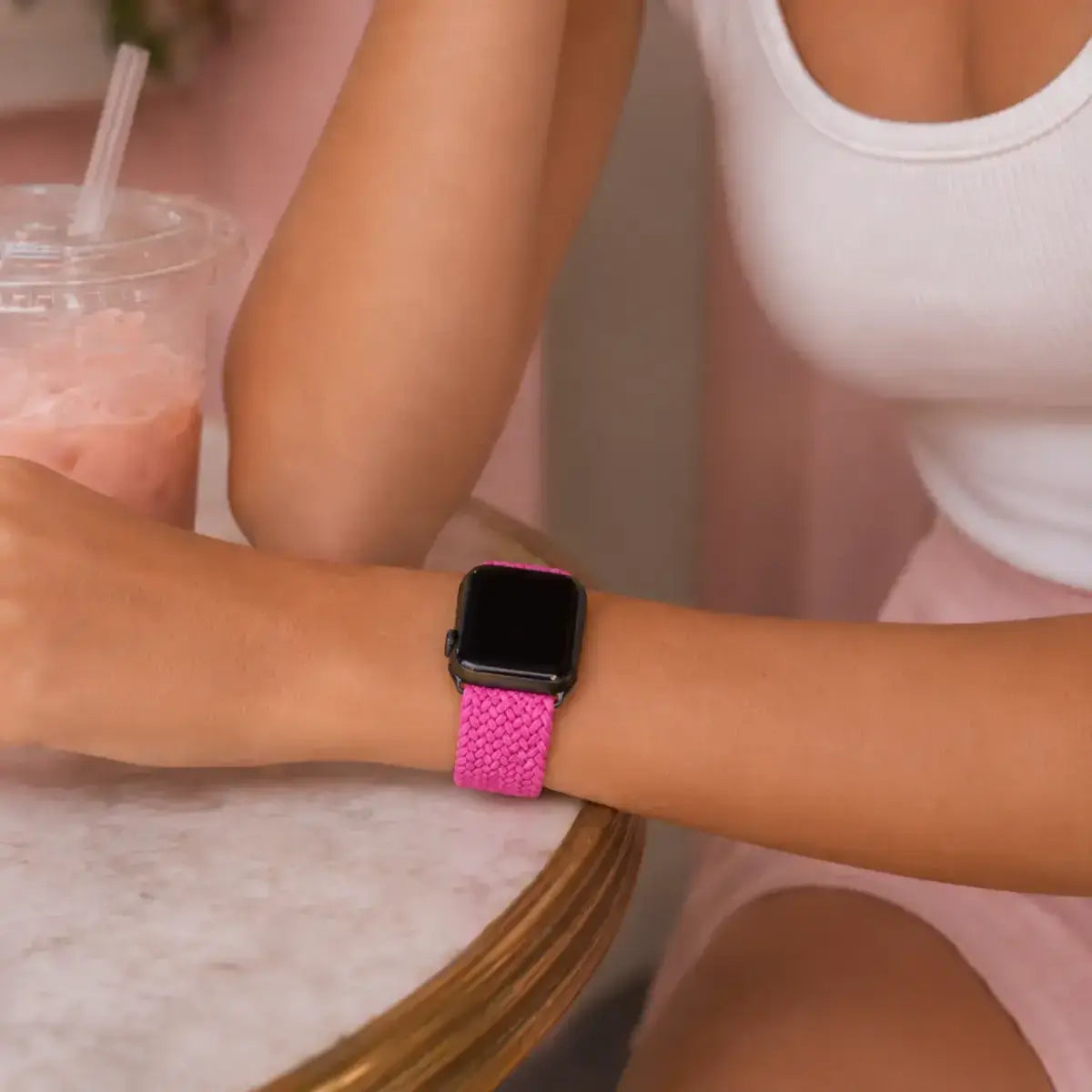 Close-up of a fuchsia braided Apple Watch band worn at a café table