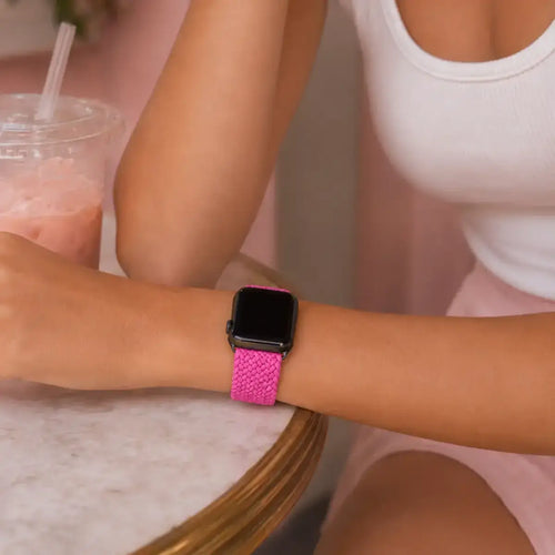 Close-up of a fuchsia braided Apple Watch band worn at a café table