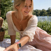 Woman wearing the Amour pink heart Apple Watch band at a sunny lakeside picnic.