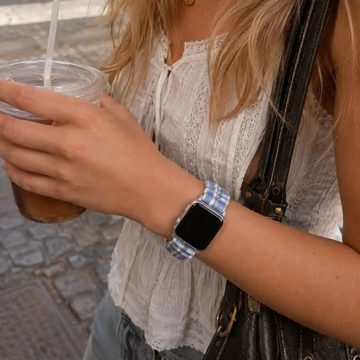 Close-up of the Camille blue gingham scrunchie Apple Watch band worn while holding an iced coffee.