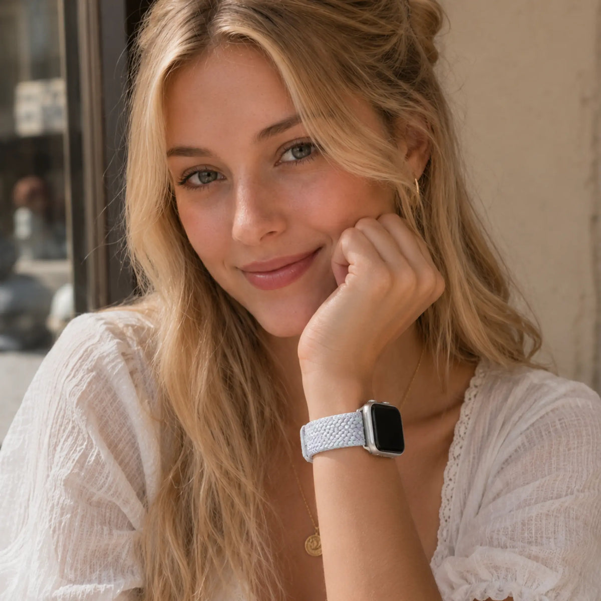 Woman wearing the Clémence blue lilac braided Apple Watch band in a café portrait.