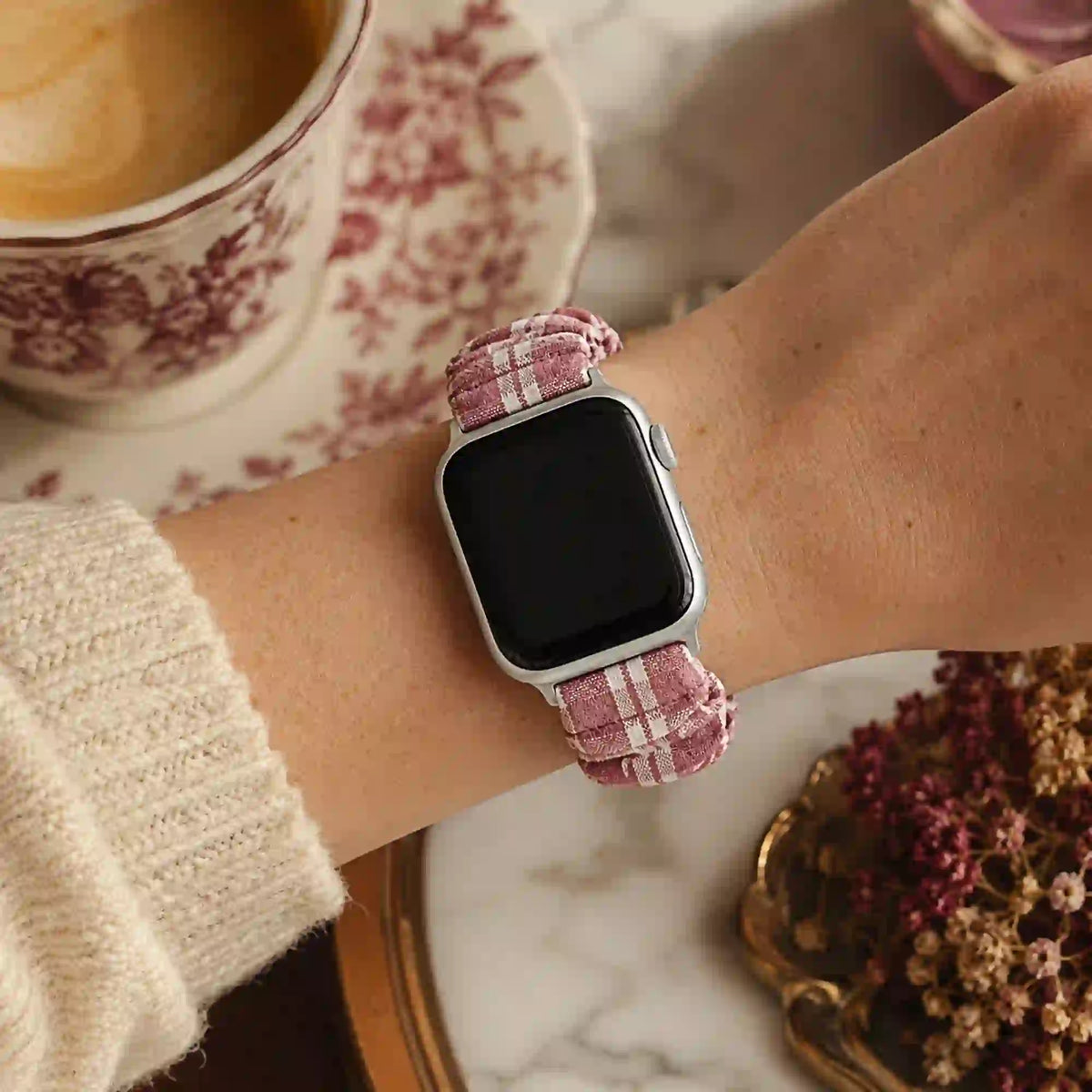 Élise burgundy gingham scrunchie Apple Watch band worn on a wrist in a café setting.