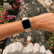 Close-up of the Luna blush silicone Apple Watch band worn along a sunlit flower garden path.