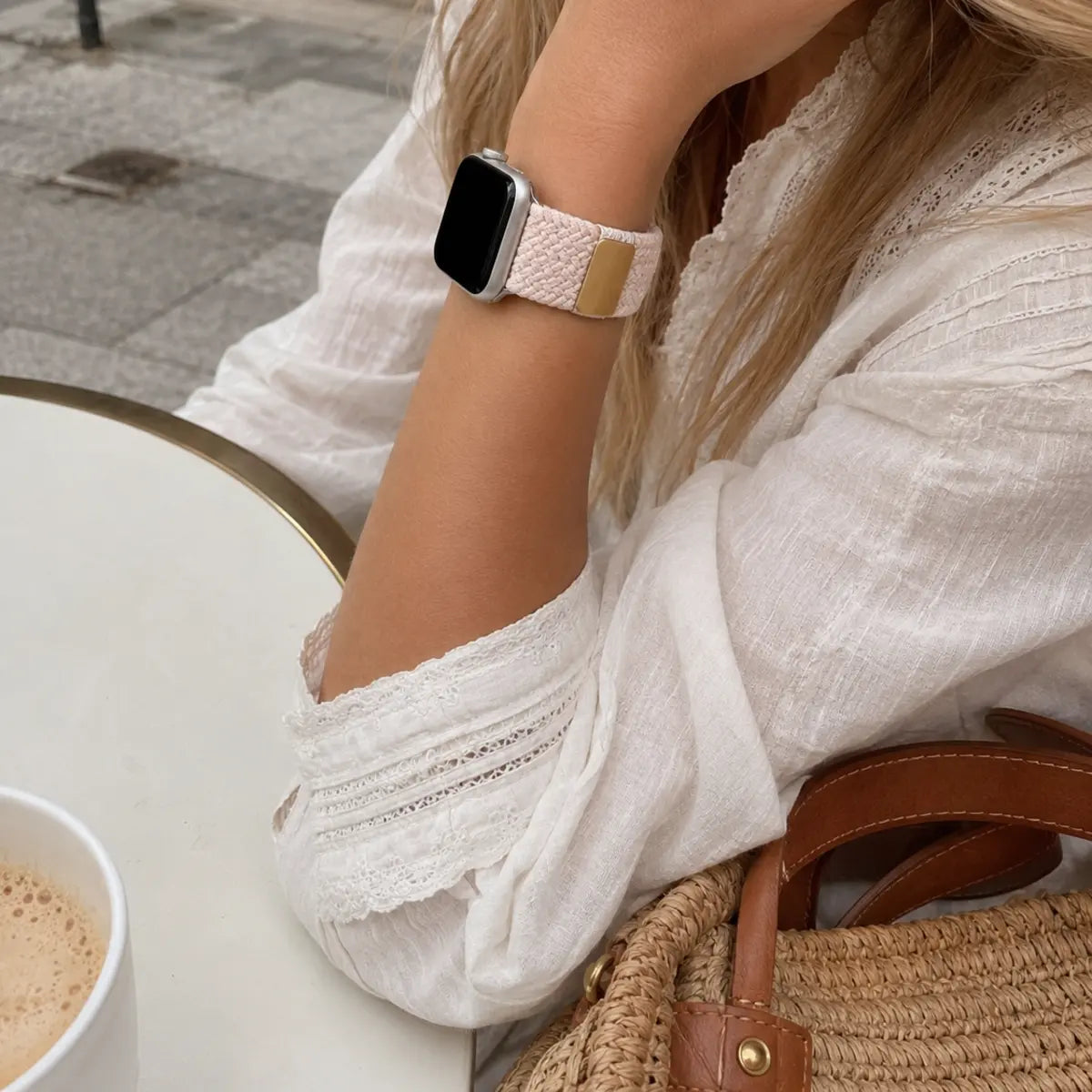 Close-up of the Margaux blush braided loop Apple Watch band at a café