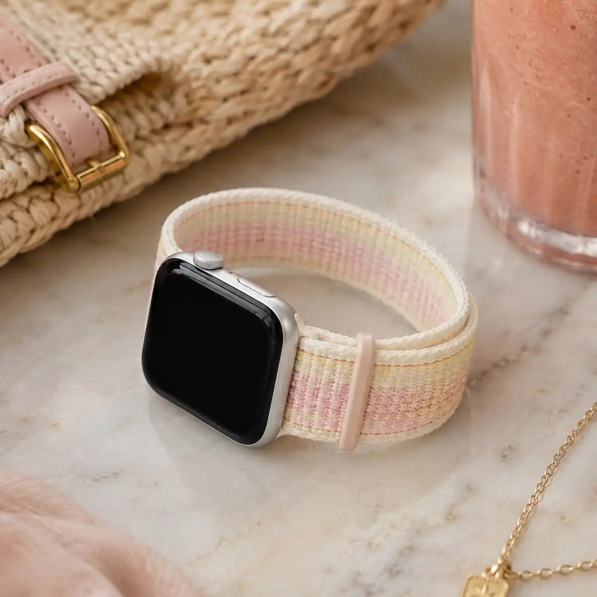 Rosalie pastel woven loop Apple Watch band displayed with a pink smoothie and woven accessories.