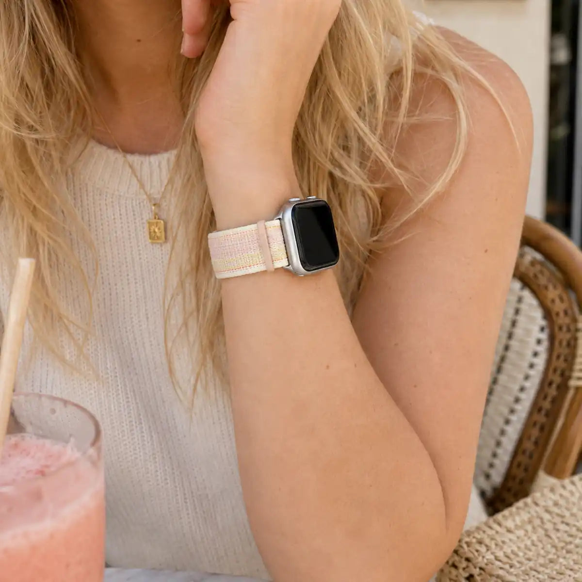Close-up of the Rosalie pastel woven loop Apple Watch band worn at a café table.
