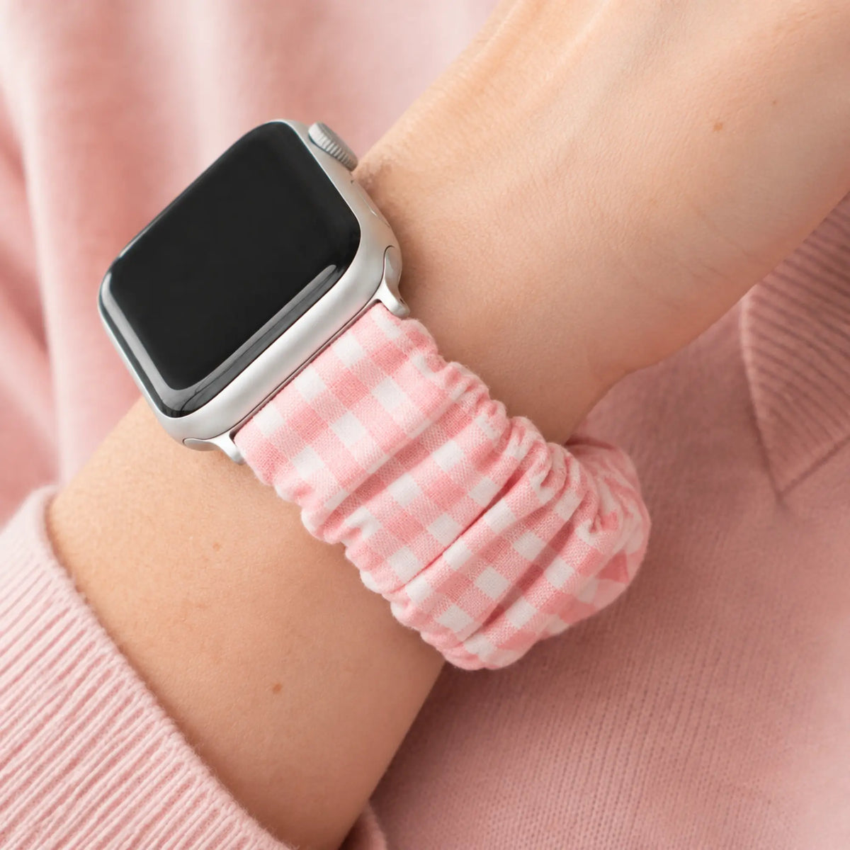 Rosie pink gingham scrunchie Apple Watch band worn on a wrist with a blush-pink knit.