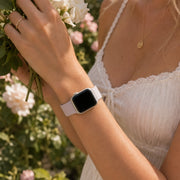 Close-up of the Violette lavender silicone Apple Watch band worn with a white lace dress in a garden.