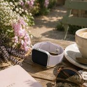 Violette lavender silicone Apple Watch band displayed beside flowers and coffee on a garden table.