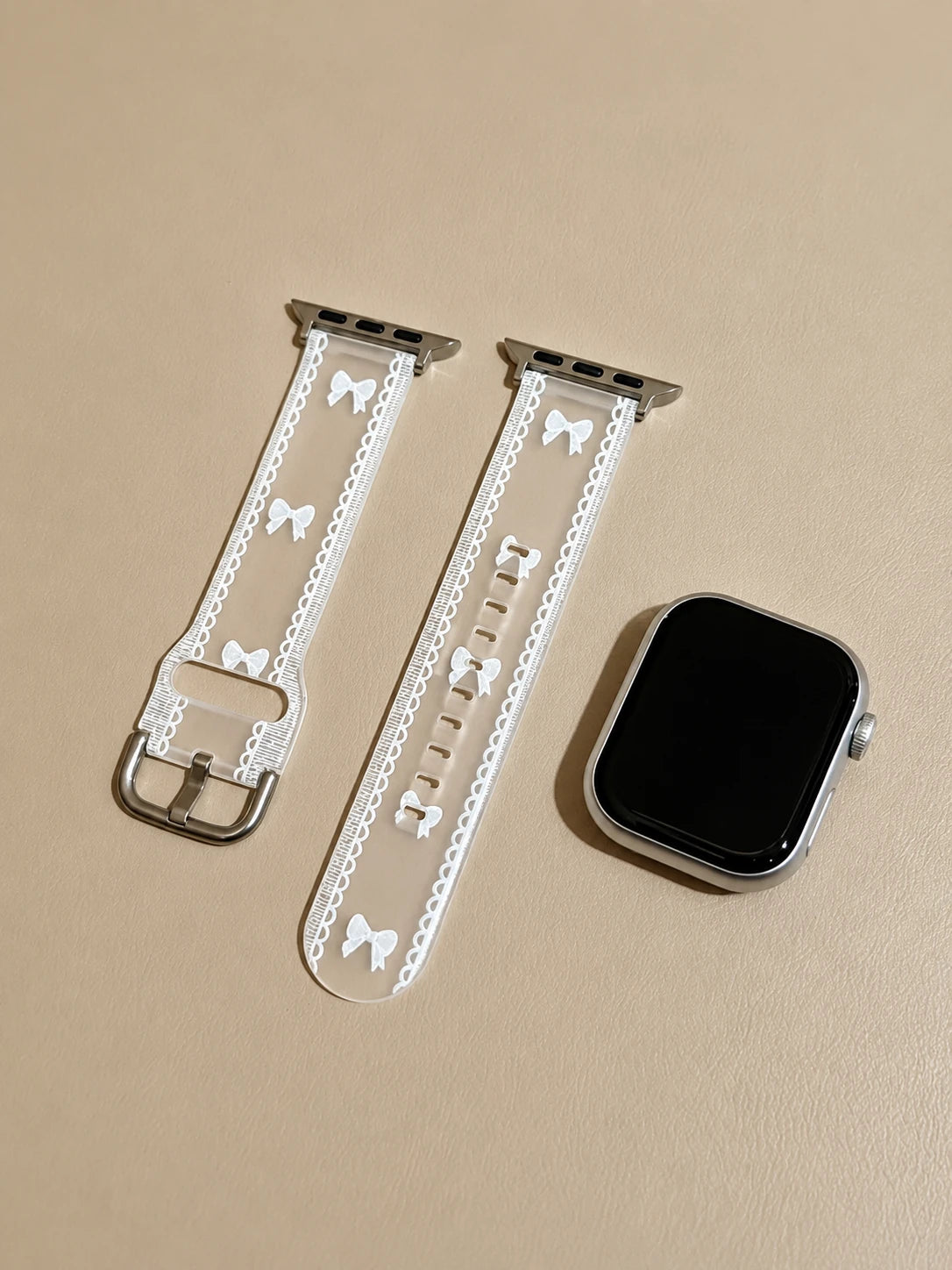 Flat lay of the Odette Clear Bow Lace Apple Watch Band and silver Apple Watch components.